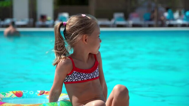 Little girl rests by hotel pool with blue water and inflatable swim ring. Summer vacation, holiday and travel