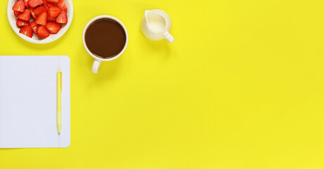 Cozy workspace. Mockup of an open notepad. Top view of a work desk, a notebook for notes, a cup of coffee, a milk jug, a pen and a plate with strawberries on a yellow background. Flat lay