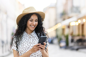 A beautiful young woman walks through the evening city in a hat, a smiling Latin American woman...