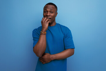 excited young smart american man in t-shirt worries on blue background with copy space