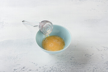 A blue bowl with a beaten egg and a whisk on a light blue table. Stage of home baking