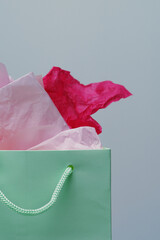 Green gift bag with pink tissue paper. Plain background.