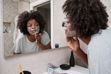 African woman washing her face skin with soap in bathroom.