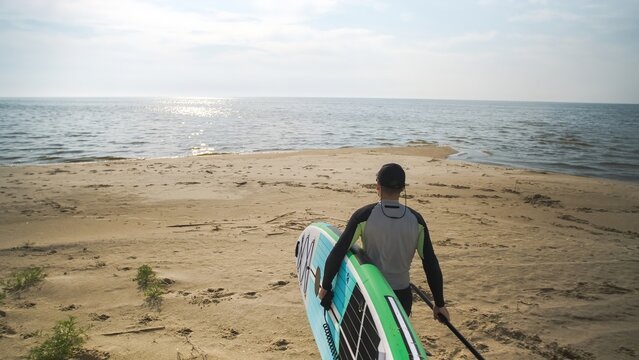 Man walking down beach to water with stand up paddle board in his hands. SUP