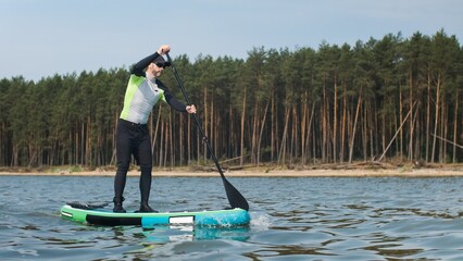 Man paddling on stand up paddle board against background of pine forest. SUP