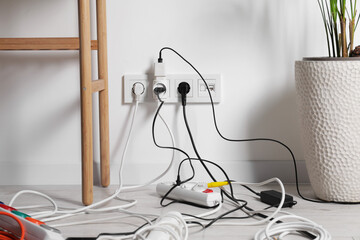 Different electrical plugs in socket and power strip on floor indoors - obrazy, fototapety, plakaty
