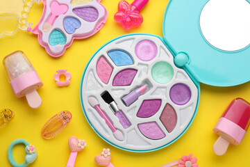 Eye shadow palette and other decorative cosmetics for kids on yellow background, flat lay