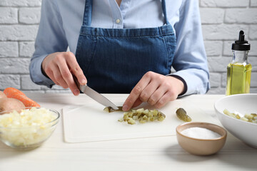 Woman cutting pickled cucumbers at white wooden table, closeup. Cooking vinaigrette salad
