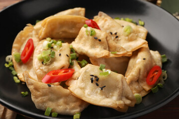 Delicious gyoza (asian dumplings) with sesame seeds, green onions and chili peppers in bowl, closeup