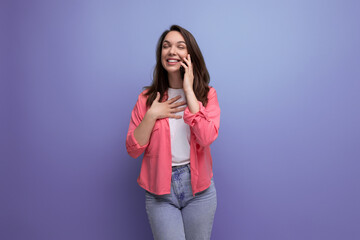 young woman in a pink shirt and jeans communicates on a mobile phone on a studio isolated background