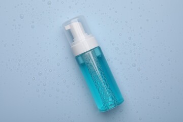 Wet bottle of face cleansing product on light blue background, top view
