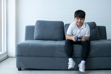Concentrated Indian boy excited playing video game, sitting on couch and holding controller having...