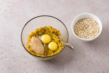 Glass bowl with crushed pumpkin, brown sugar, eggs and a bowl of oats on a beige textured background. Cooking delicious healthy homemade autumn pastries