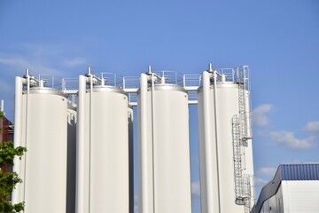 Four white towers of a modern milk processing plant against a blue sky.