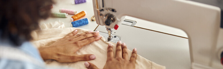 African-American worker sews white fabric with machine tool at t