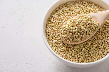 Organic raw green buckwheat in wooden spoon in white bowl on white background. Close up. Copy space.