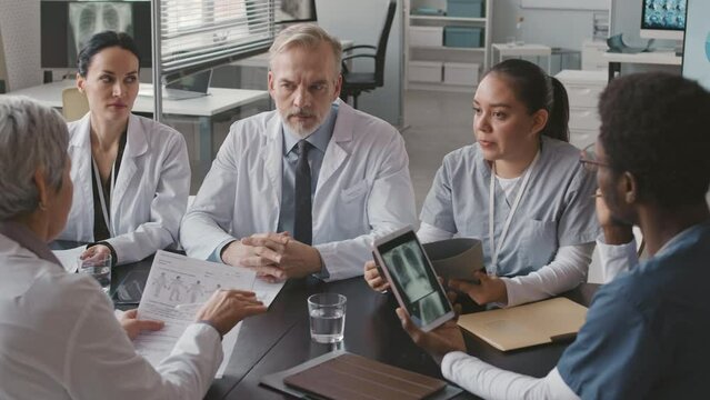 Waist up of multiethnic group of doctors and mature Caucasian male chief physician having meeting in contemporary medical clinic