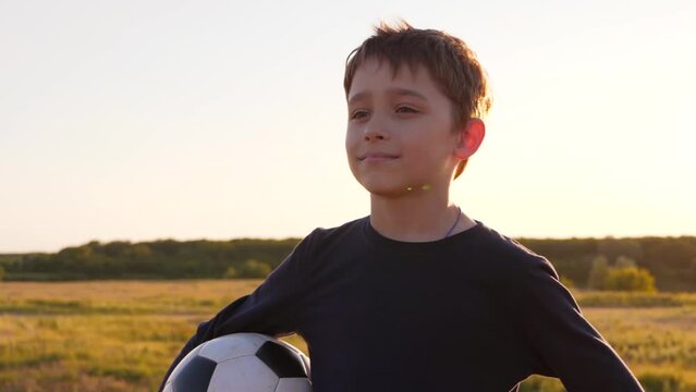 Portrait of a happy boy on the background of sunset. A child with a soccer ball in his hands. kids dreams of sports