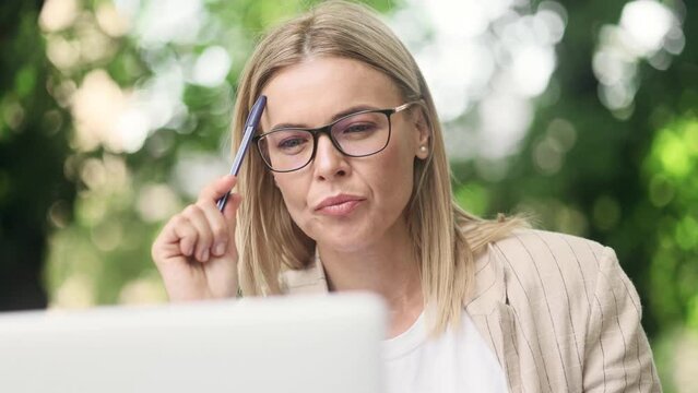 Portrait of mature blond woman thinks questioningly finding solution and writing in notebook at city street cafe Successful businesswoman Idea pointing forward index finger concept