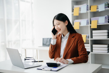 Business asian woman Talking on the phone and using a laptop with a smile while sitting in office