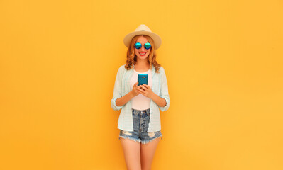 Happy smiling young woman 20s with smartphone wearing summer straw hat, shorts on yellow background