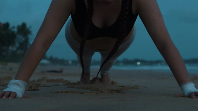 Female boxer MMA fighter girl doing push-ups on beach at sunset sunrise.