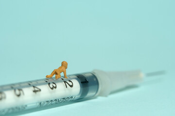 Miniature tiny people toy figure photography. An infant baby crawling above syringe. Isolated on blue background