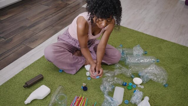African American woman sorting garbage while sitting on the floor at home