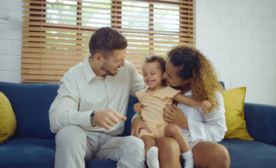 Happy cheerful parents having fun with cute daughter and hugging on sofa together, Enjoying family lifestyle at home concept.