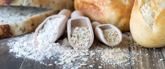 Wooden scoops of wheat flour, oats and oat bran with bread and buns in behind.