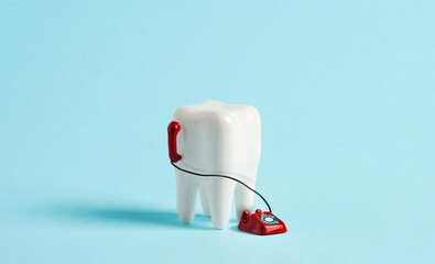 Model of human tooth with miniature phone on blue background. Call center dental clinic advertising...