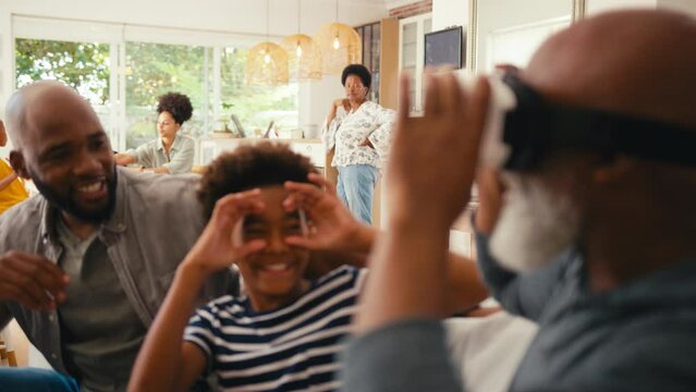 Grandfather wearing VR headset is amazed as he sits with multi-generation male family on sofa at home together - shot in slow motion