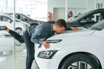 Kissing the new automobile. Handsome car dealership worker is with electric vehicle