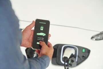 Charging process on the smartphone app. Close up view of man that is with electrical car