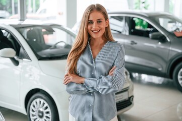 Standing with arms crossed. Beautiful woman is indoors with the modern car