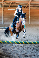 Pretty young girl doing equestrian show jumping on her pony in a farm - 617789032