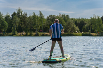 A man on a sup board floats on a lake on a summer day.