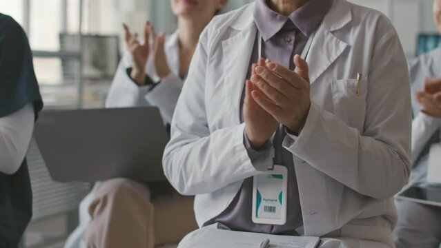 Cropped shot of group of doctors in white lab coats clapping after listening lecture at open medical seminar