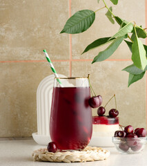Cherry juice in a transparent glass and fresh cherries on a white table