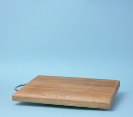 Wooden empty cutting board at an angle on a blue background, kitchen utensils