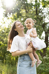 A mother spends time with her two-year-old daughter. Mother and daughter are walking in the garden, hugging and having fun. Mother and her daughter. Maternal love and attachment. Tenderness. 