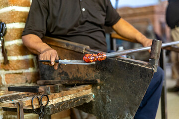 Craftsman working, cutting and molding the glass with the traditional method of glass blowing which...
