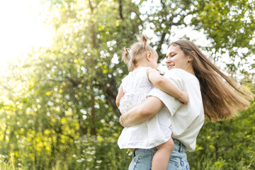 A mother spends time with her two-year-old daughter. Mother and daughter are walking in the garden, hugging and having fun. Mother and her daughter. Maternal love and attachment. Tenderness. 