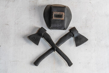 Two crossed black axes and a protective mask for welding on a white stucco wall, closeup