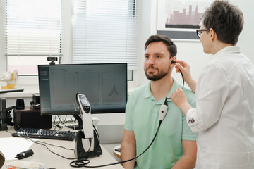 Man has appointment at clinic, checking hearing. Doctor audiologist consulting at hearing rehabilitation clinic to select digital device for middle age man. Doctor consulting patient