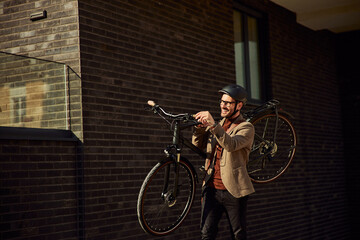 A cheerful businessman with a helmet carrying his bicycle on the street.
