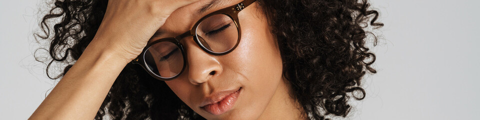 Black curly woman in eyeglasses with headache holding her forehead