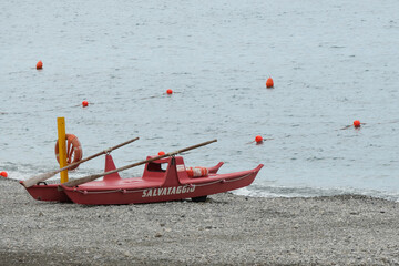 Un pattino di salvataggio rosso in riva al mare. - obrazy, fototapety, plakaty