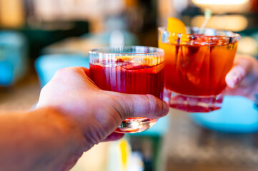 hands of man and woman holding and clinking glasses cocktails in restaurant