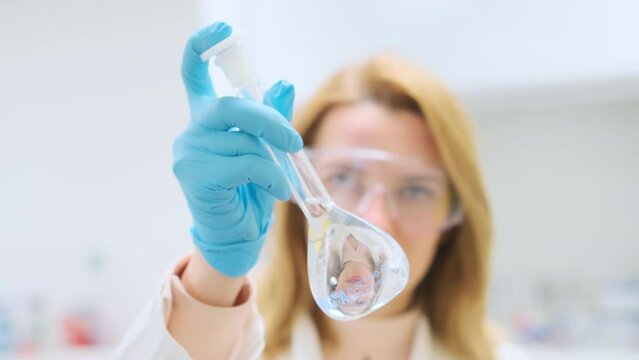 Female scientist in protective goggles shakes a glass flask preparing solutions in the laboratory 